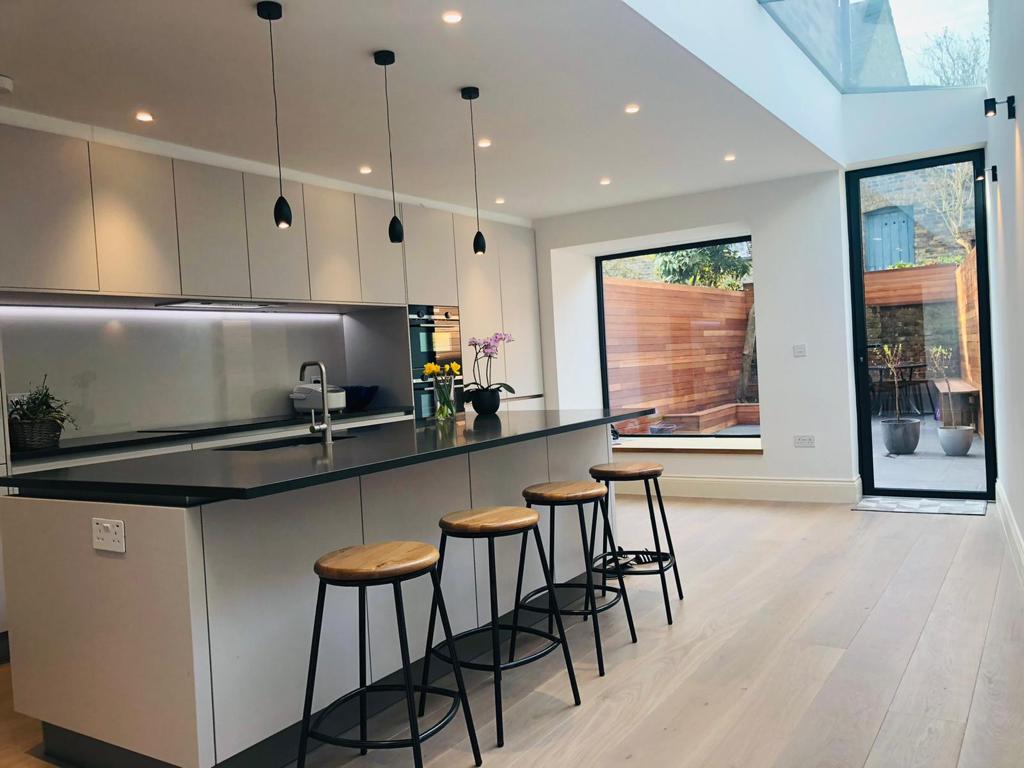 Open-plan handleless kitchen extension with long skylight, black pendant lights and bifold doors onto a cedar-clad garden
